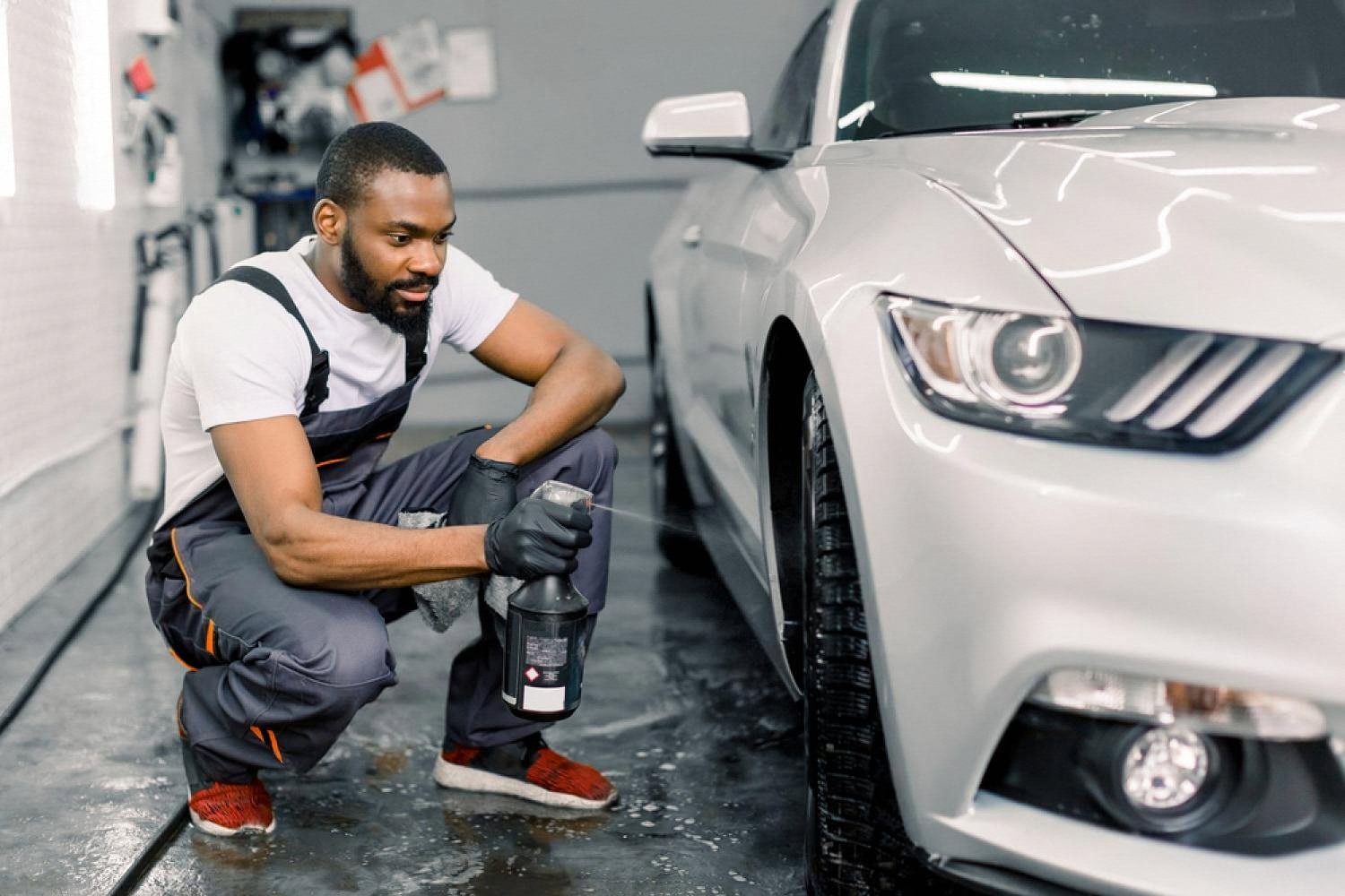 Detailer spraying rim protection sealant on a silver car wheel in a UAE detailing bay