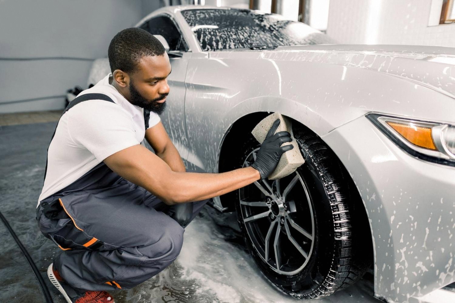 Detailer washing a car rim with a sponge and foam during a UAE car wash